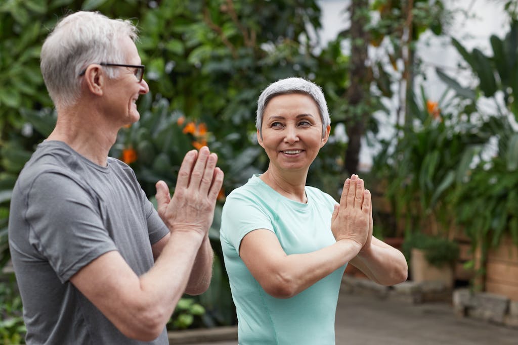 Happy senior couple practicing yoga in a lush greenhouse setting, embodying wellness and togetherness.